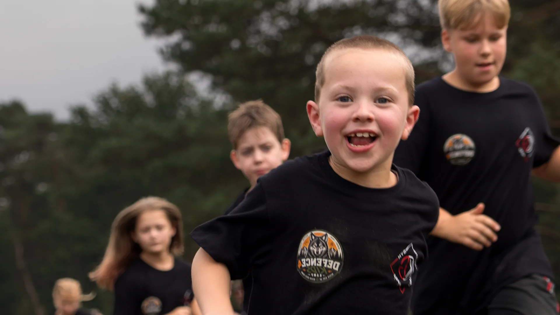 Een lachende jongen in een Defence4Kids-shirt rent vooraan, met de rest van de groep achter zich op de heide