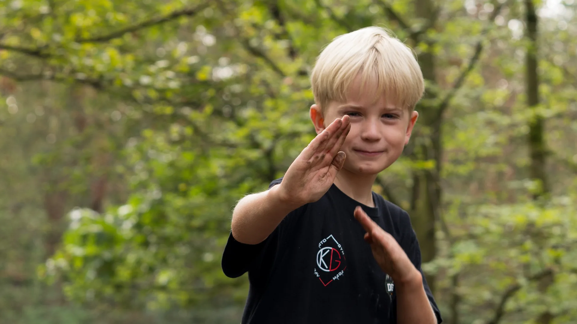 Een jongen in een Kamato-shirt staat in gevechtshouding met zijn handen omhoog, op een bospad