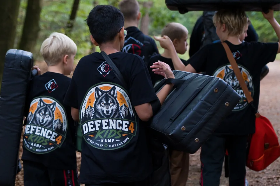 Kinderen dragen stootkussens over een bospad tijdens het Defence4Kids-kamp