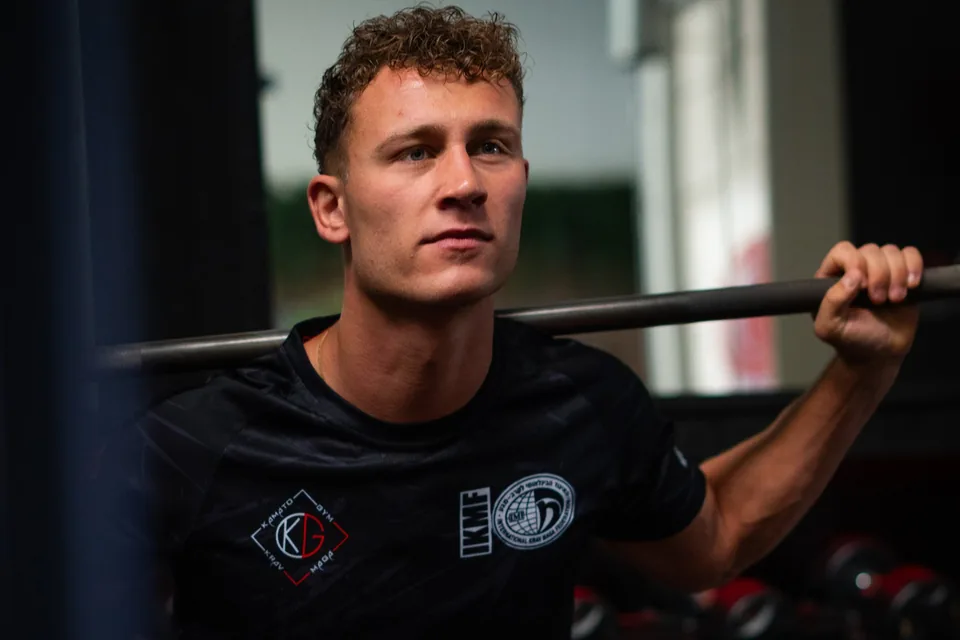 Een cursist tilt een halterstang op zijn schouders in de krachtruimte
